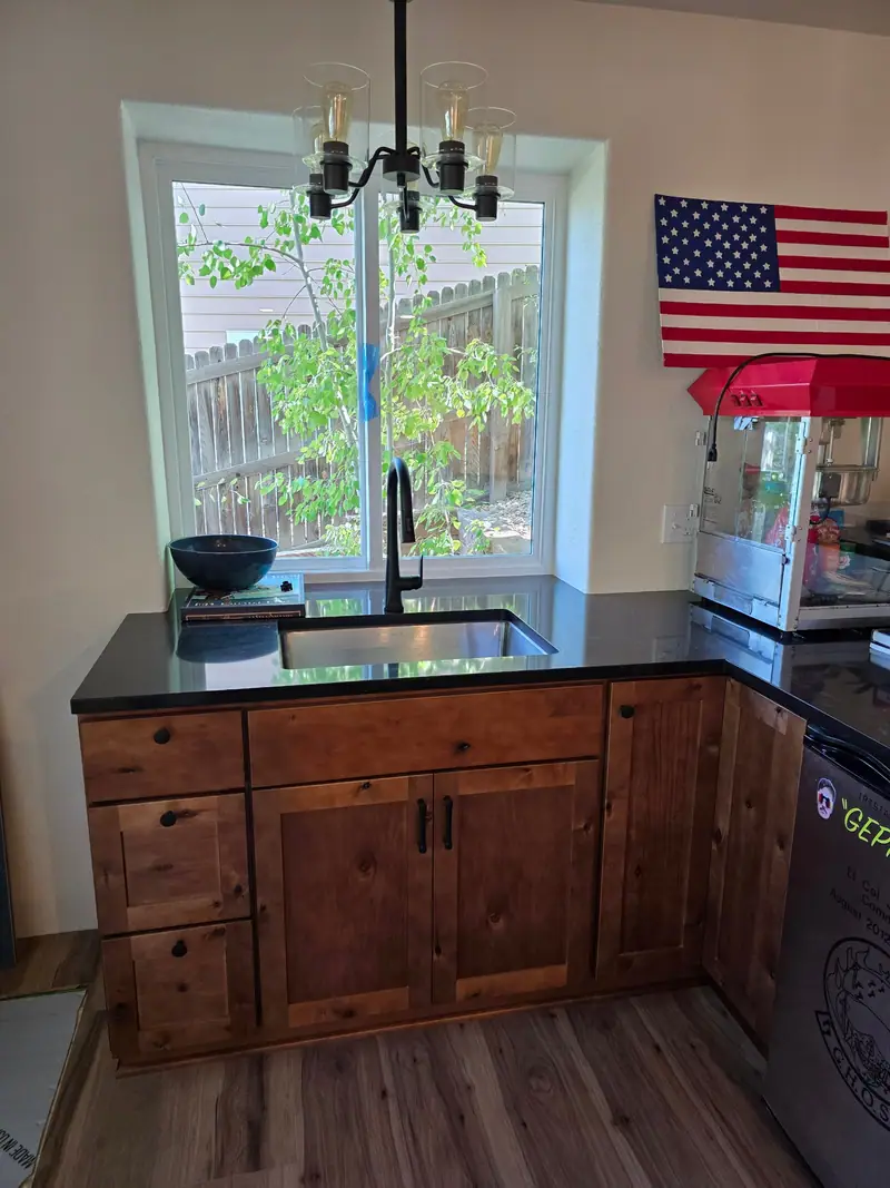 Finished basement bar with alder cabinets, black stone counter and an undermount sink under a window