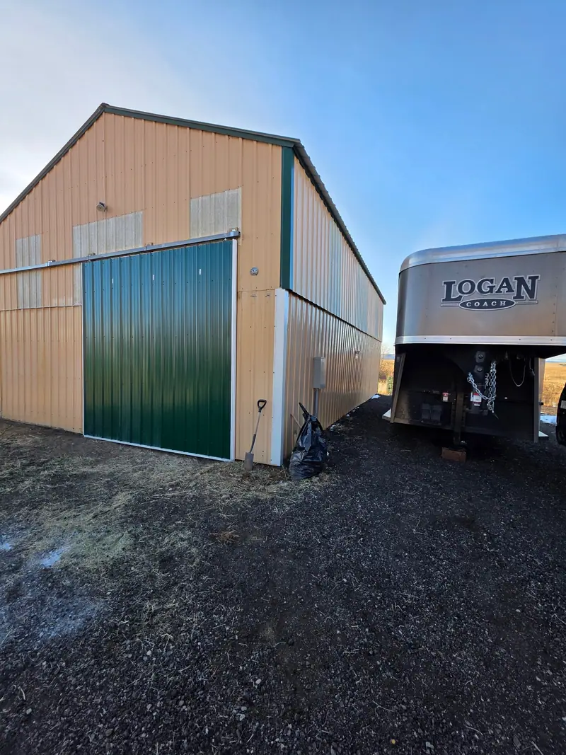 Tan metal pole barn with a green sliding door