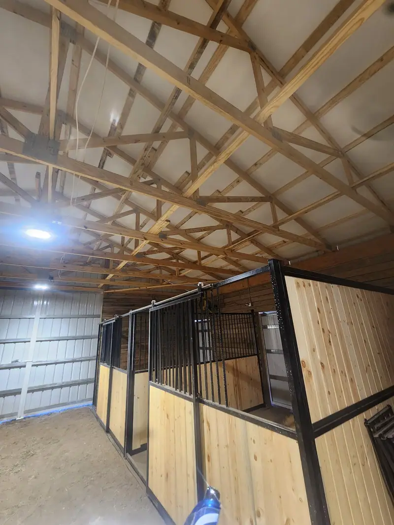 Horse stalls inside a pole barn with tongue-and-groove wood walls and black steel grille tops