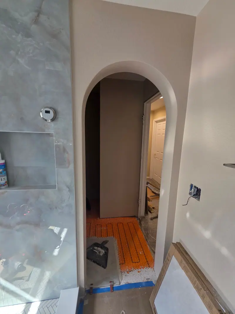 Bathroom remodel with an arched doorway, floor-heating mat laid before tile and marble-look wall tile with a niche