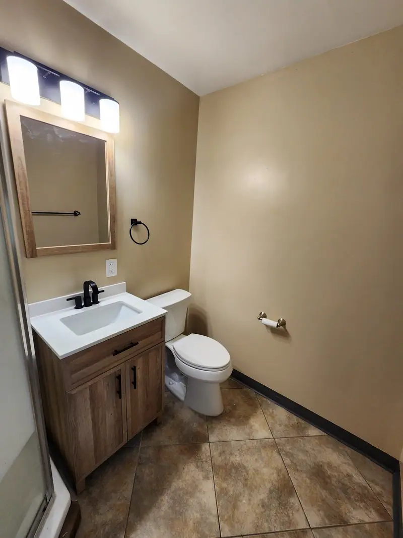 Small finished bathroom with wood vanity, black faucet, tile floor and vanity light