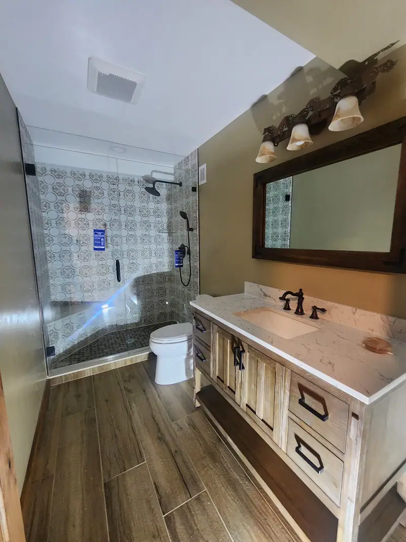 Remodeled bathroom with frameless glass walk-in shower, patterned tile, wood vanity and marble-look top