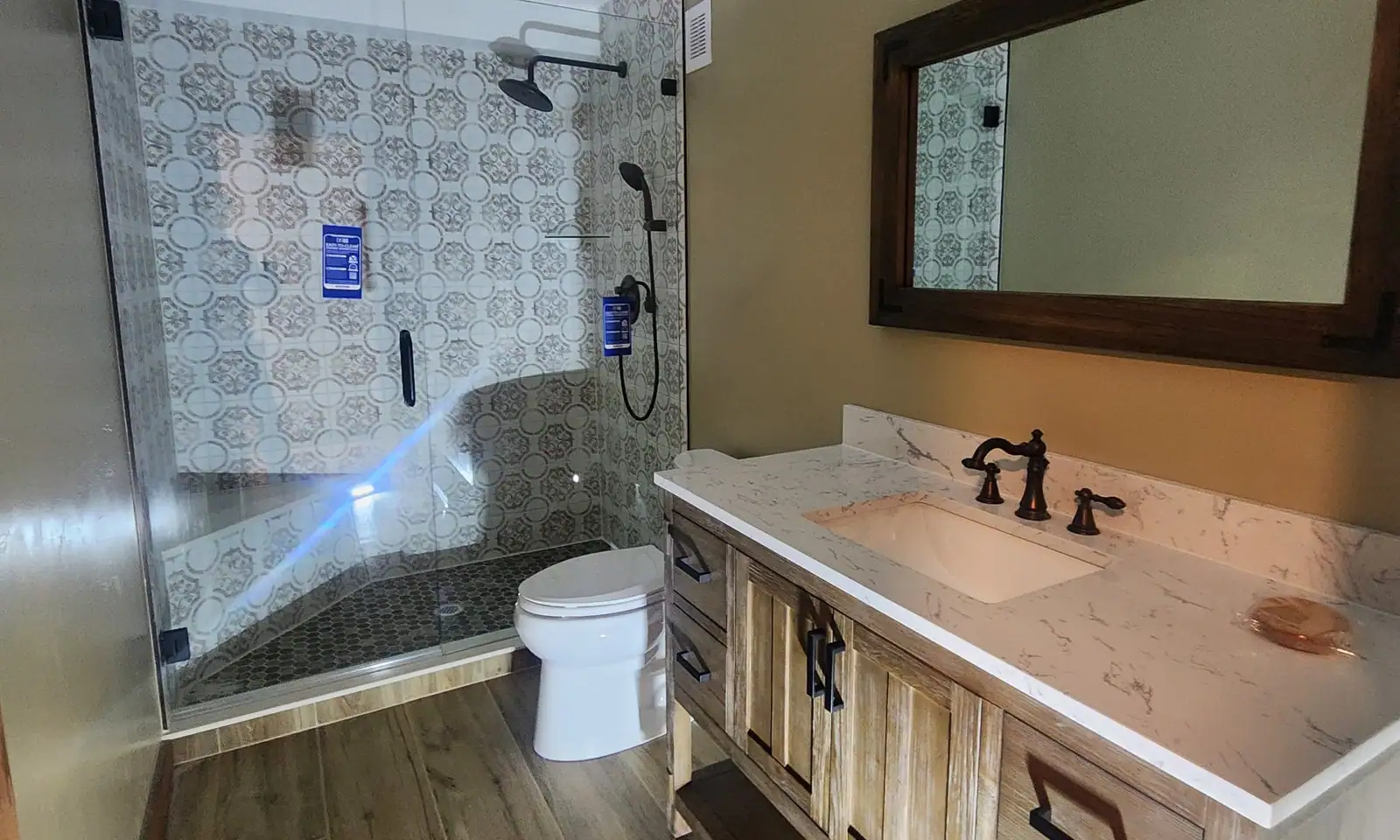 Remodeled bathroom with frameless glass walk-in shower, patterned tile, wood vanity and marble-look top