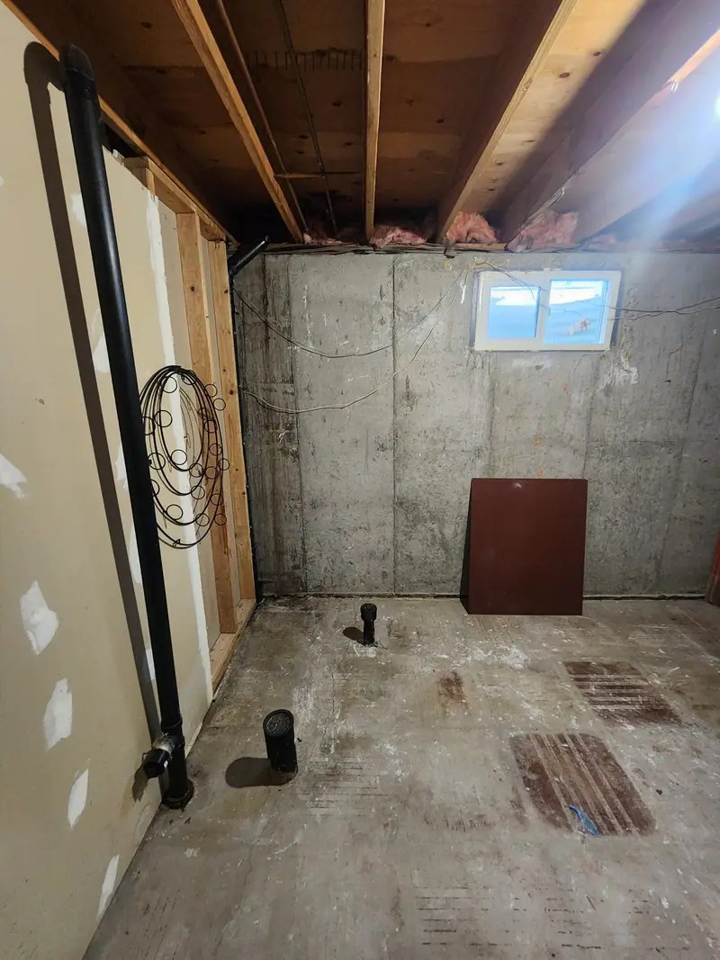 Unfinished basement corner with bare concrete walls and open joists before a remodel