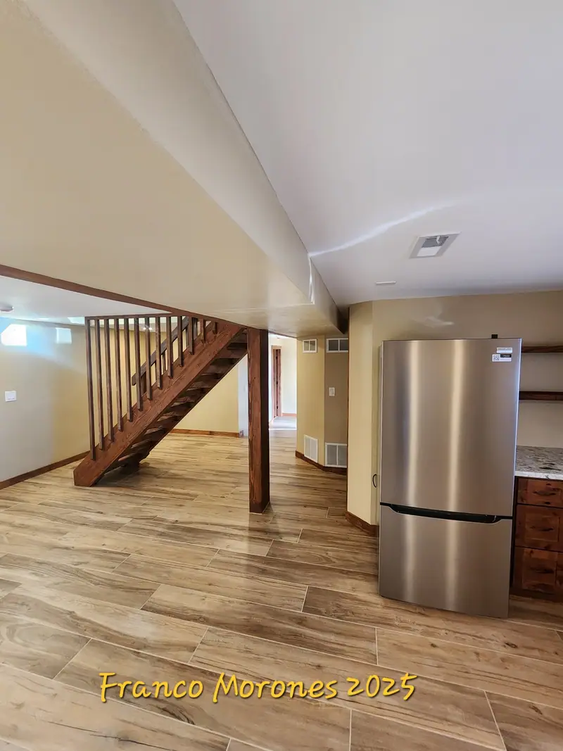 Finished basement room with wood stair, stainless refrigerator and plank flooring