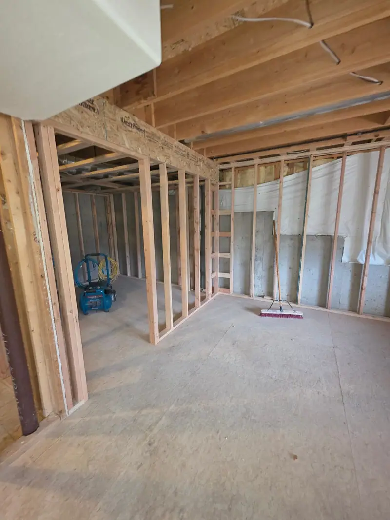 Basement framing with new stud walls under open joists on a concrete floor