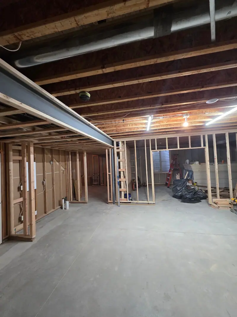 Basement framing in progress with stud walls, a steel beam and open ceiling joists