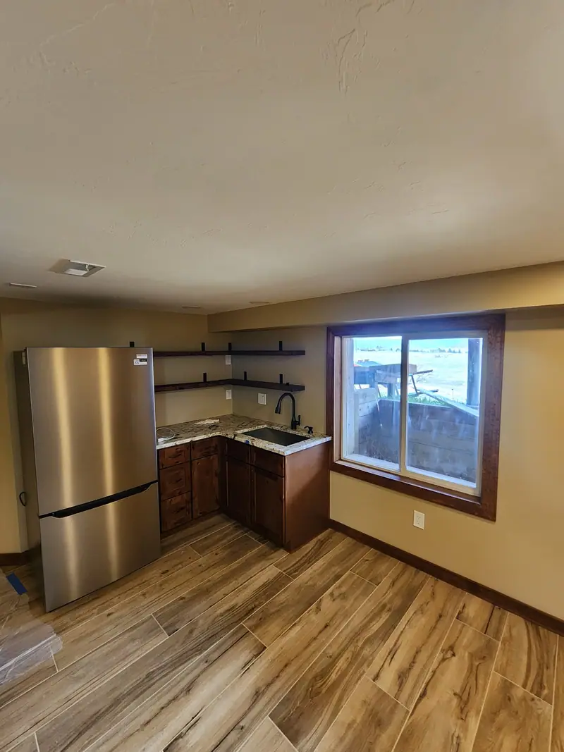 Basement kitchenette with stainless fridge, wood cabinets, granite top and open shelving by a window