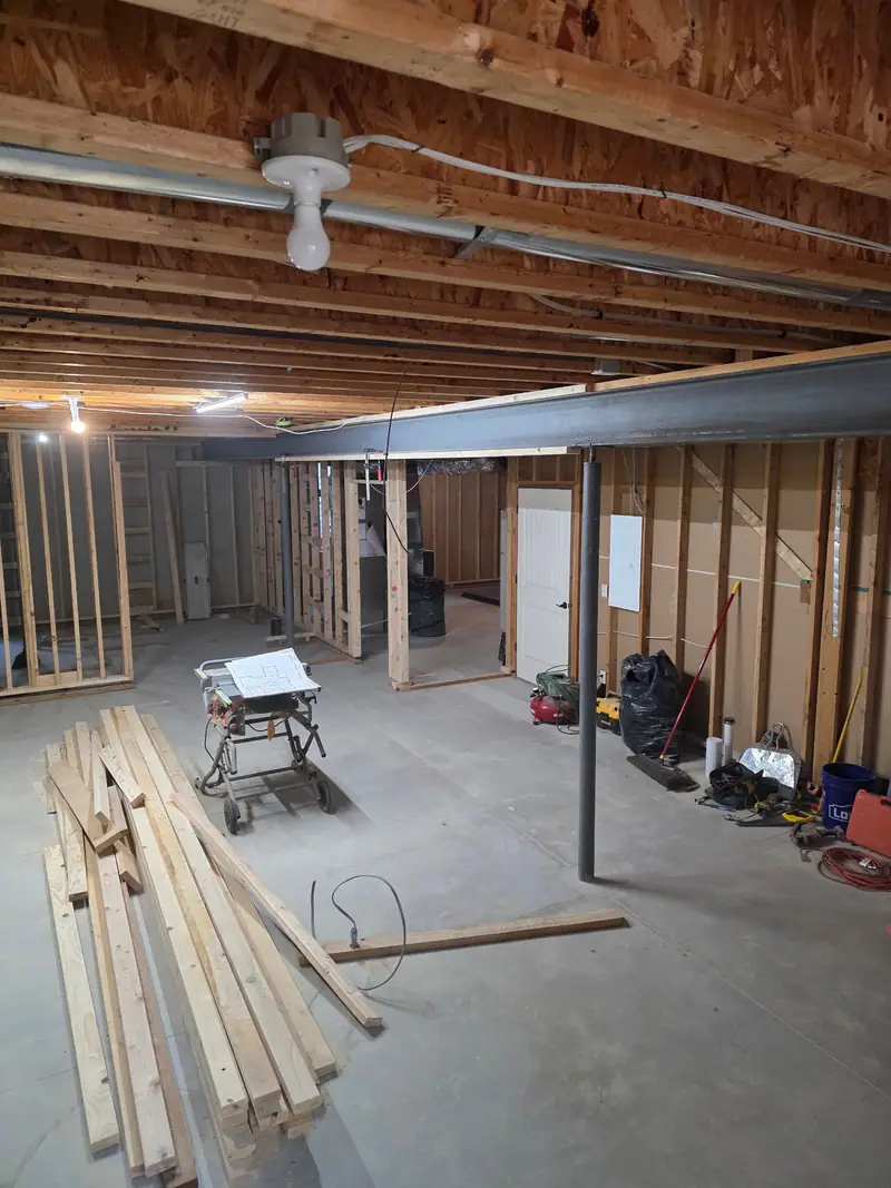 Unfinished basement with lumber stacked and a table saw set up before framing