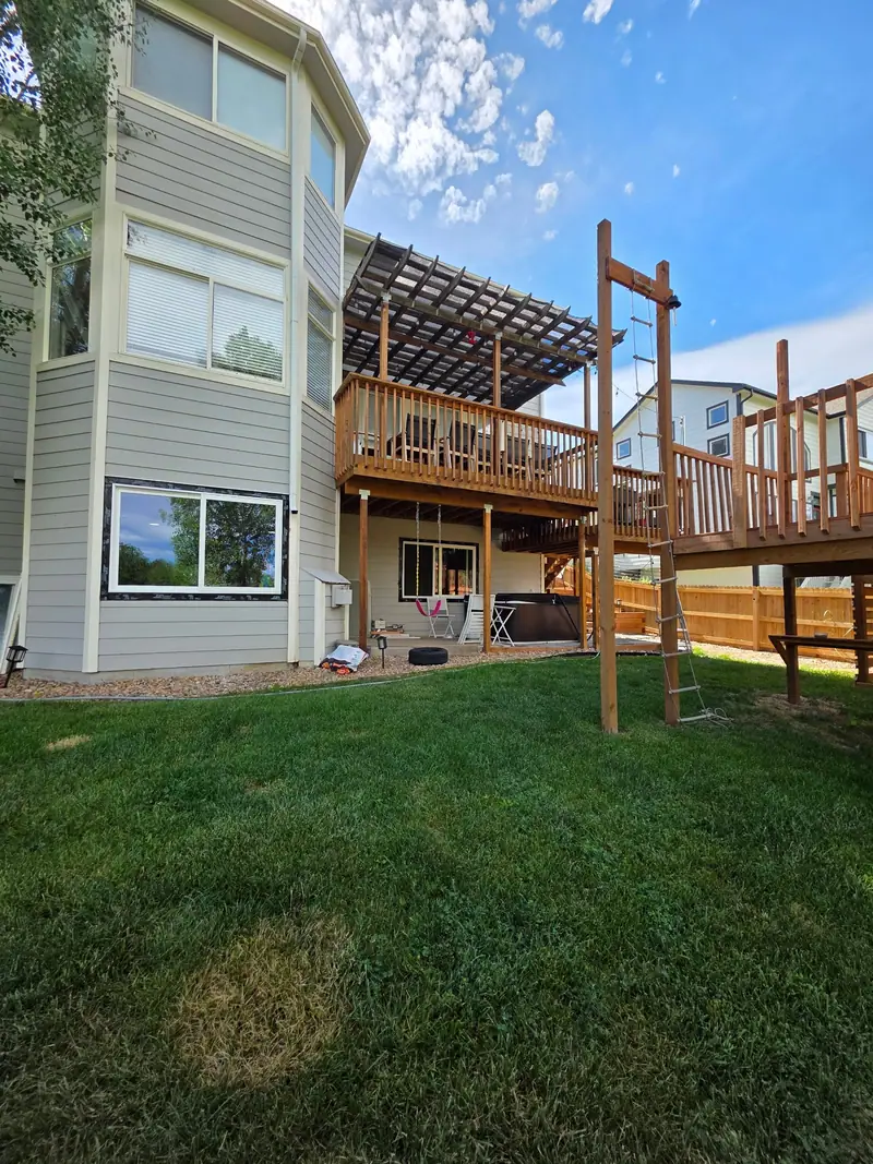 Two-level wood deck with a pergola on the back of a grey-sided house