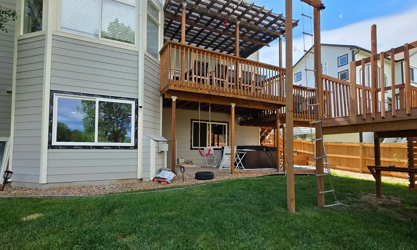 Two-level wood deck with a pergola on the back of a grey-sided house