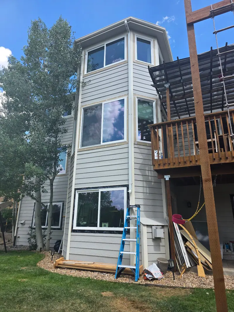 Grey-sided house with a three-story bay of new windows and a deck