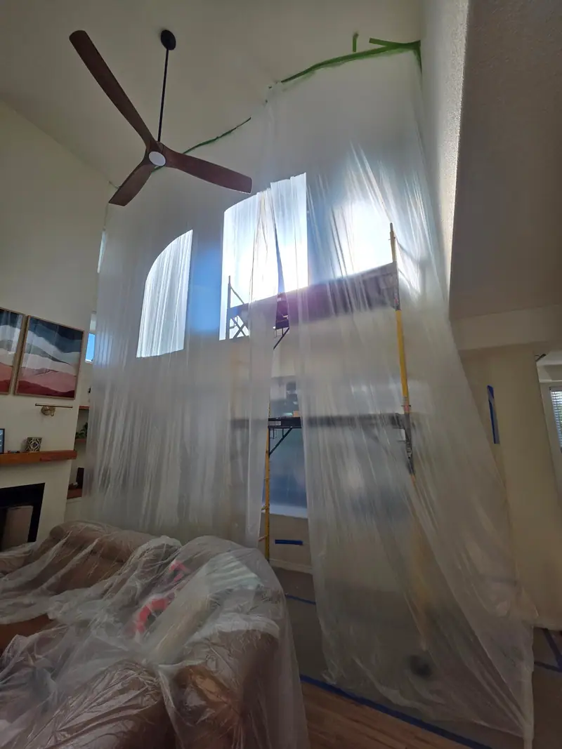 Two-story great room wrapped in plastic sheeting during a remodel
