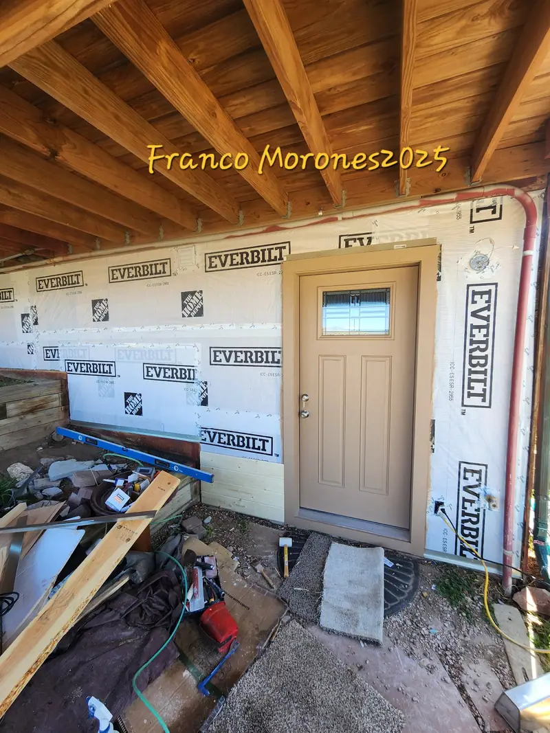 Exterior wall wrapped in house wrap with a new door installed under a deck