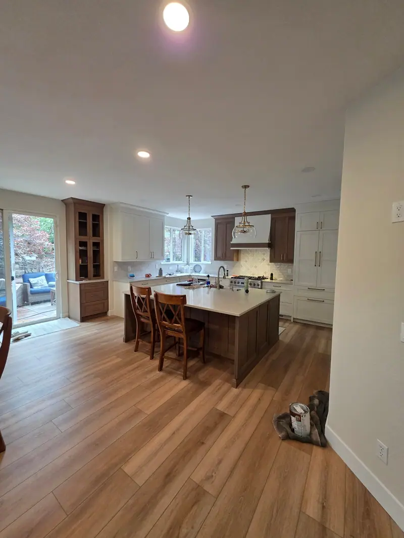 Open kitchen remodel with a walnut-stained island, bar stools, painted cabinets and new plank flooring