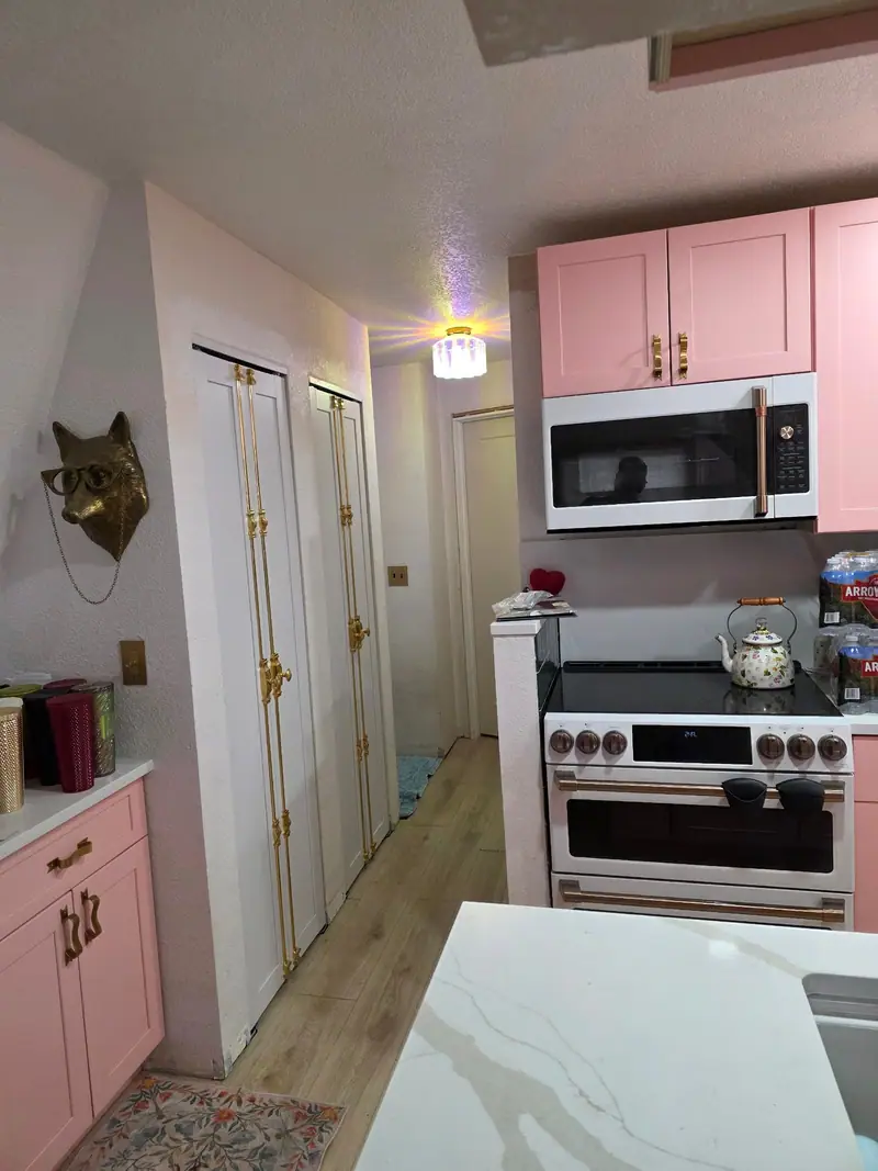 Small kitchen with pink cabinets, white stone counters and a stainless range