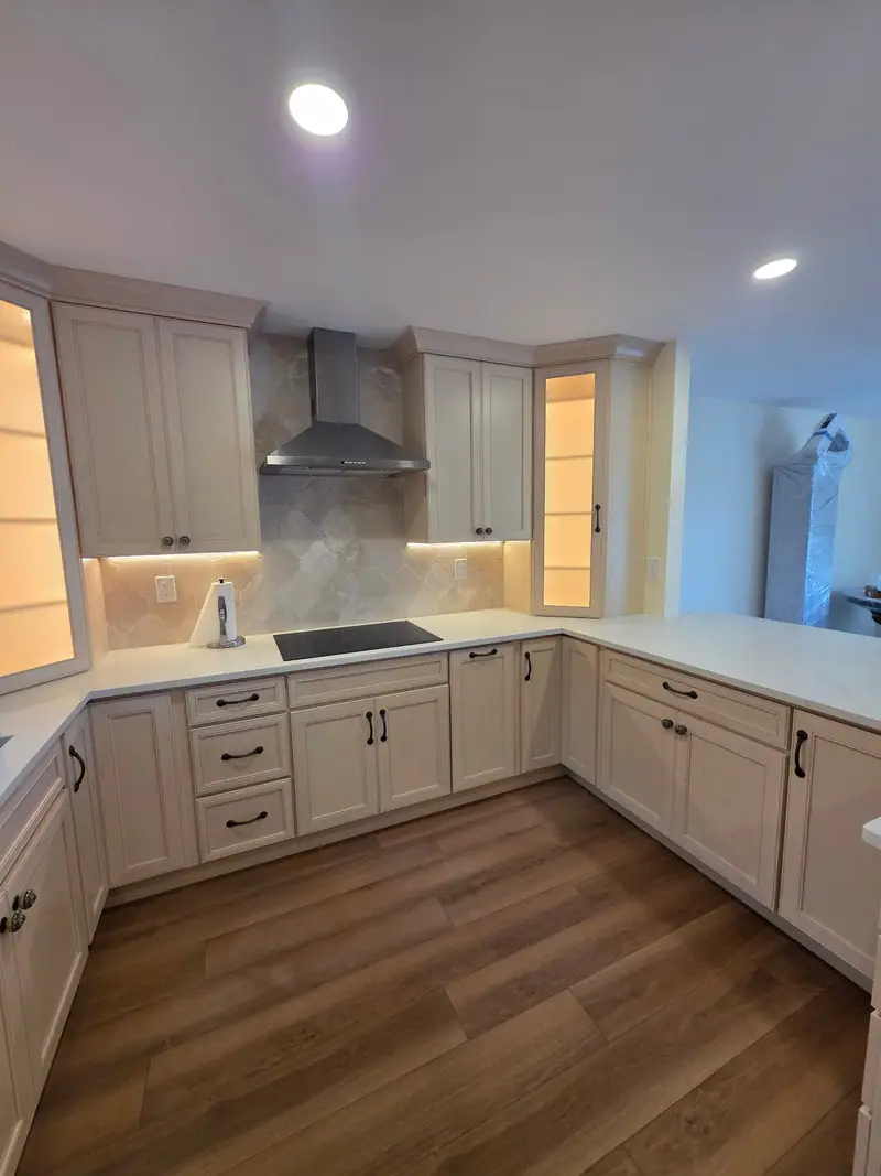 Remodeled kitchen with white shaker cabinets, under-cabinet lighting, stainless range hood and plank floor