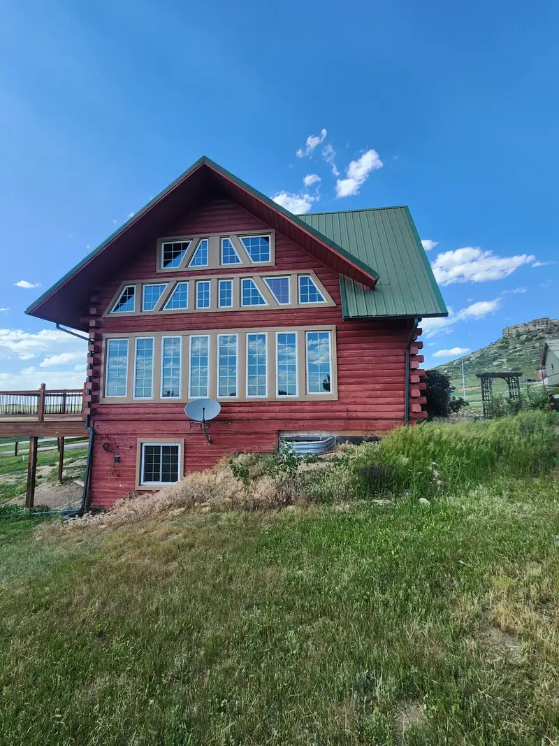 Red log home with a green metal roof and tall gable windows on a grassy hillside