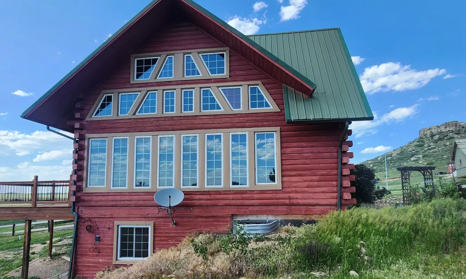 Red log home with a green metal roof and tall gable windows on a grassy hillside