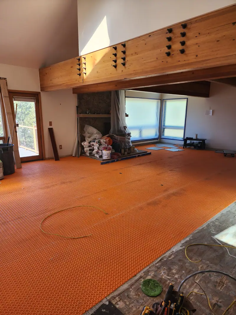 Room with orange tile underlayment membrane across the floor before tile, under a wood beam