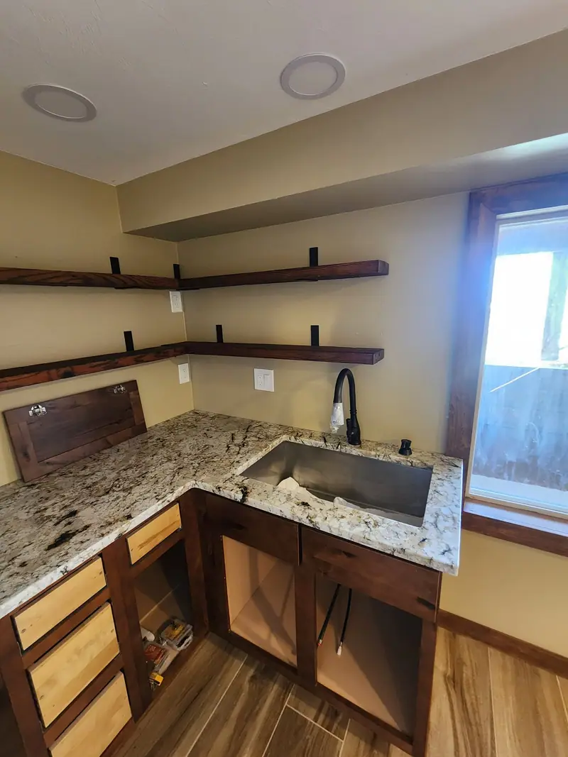 Basement kitchenette with granite countertop, wood cabinets and black-bracket floating shelves