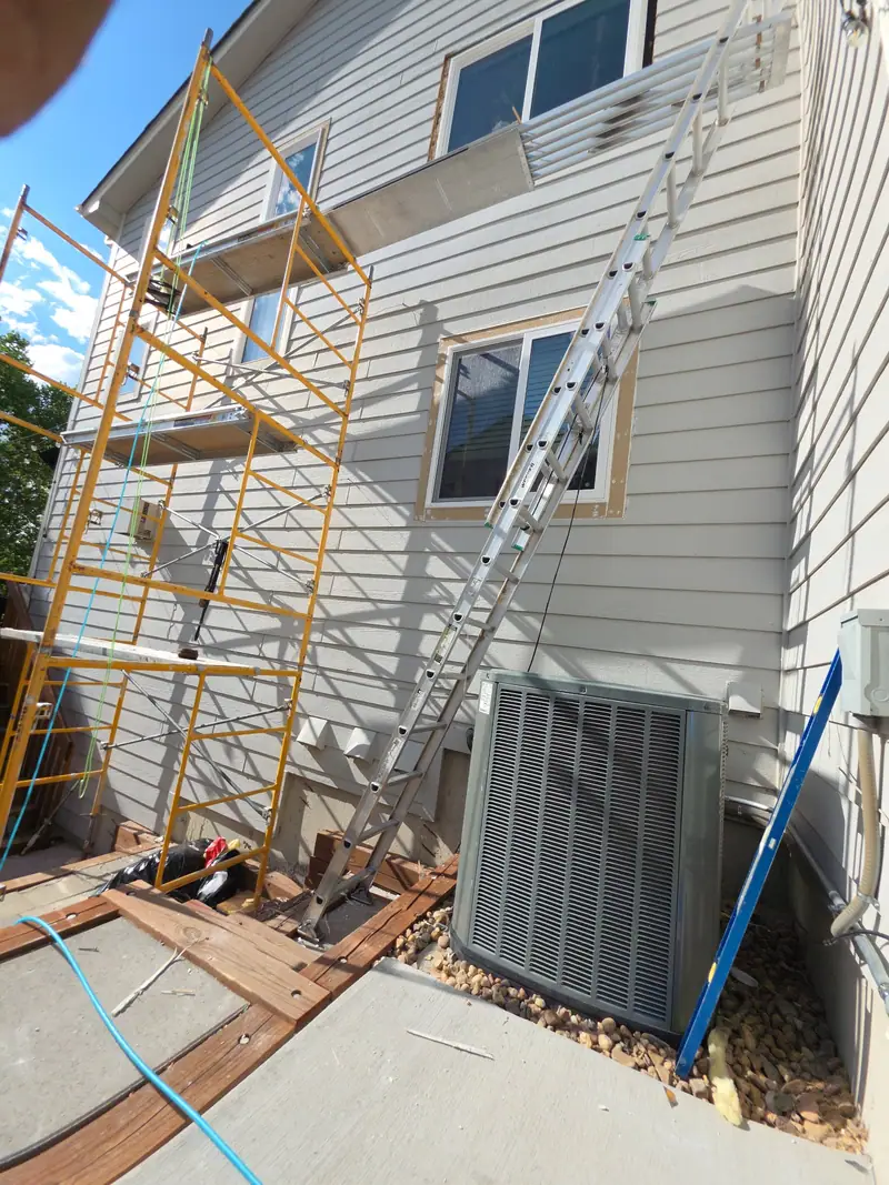 Scaffolding against a grey-sided house during exterior siding and window work