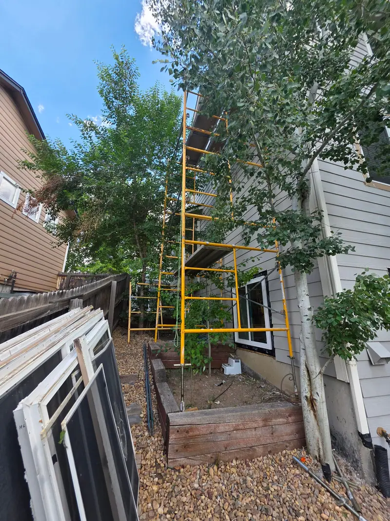 New window units stacked beside a house with scaffolding for exterior work